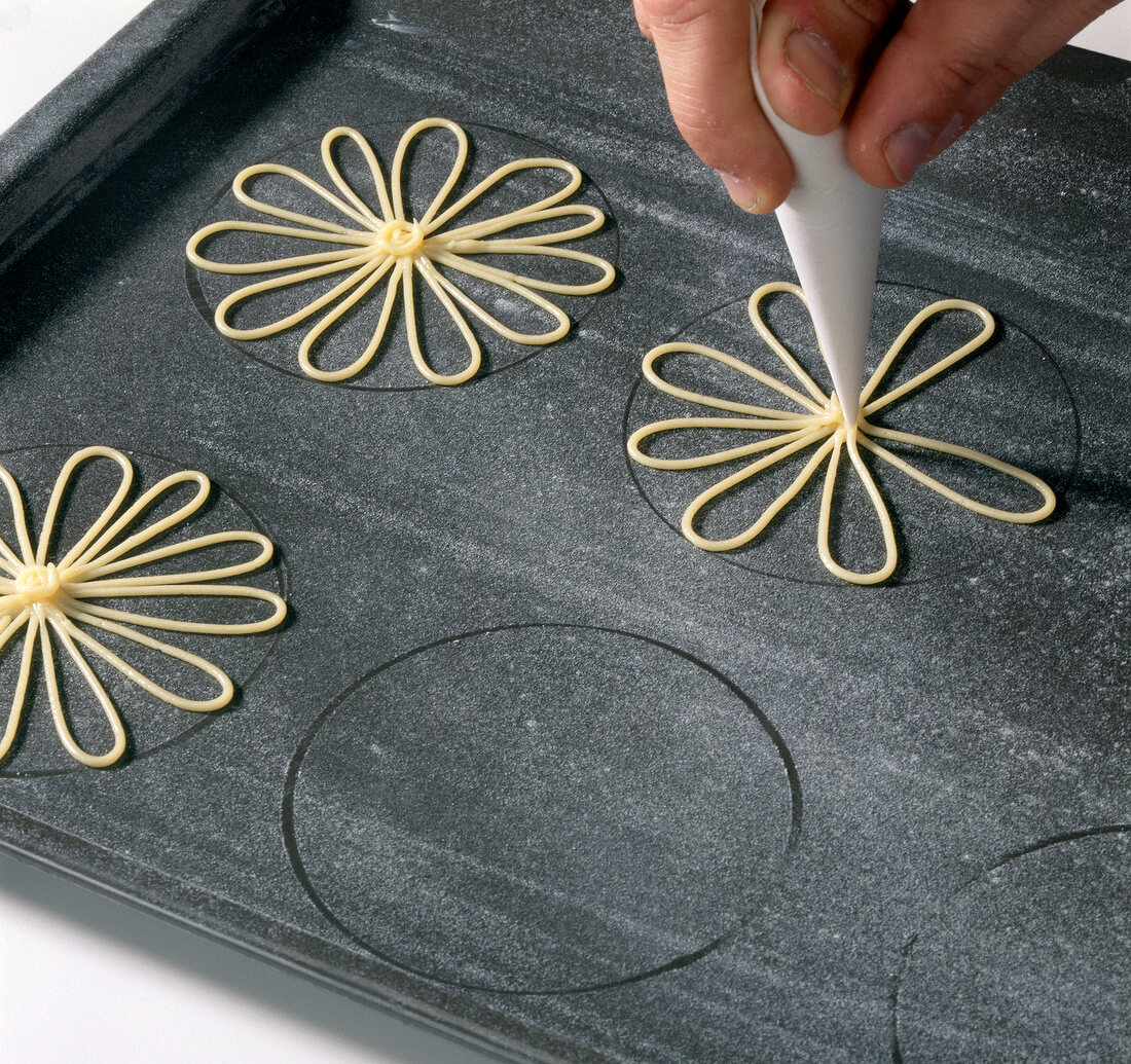 Hand making choux dough flowers with piping bag on baking sheet