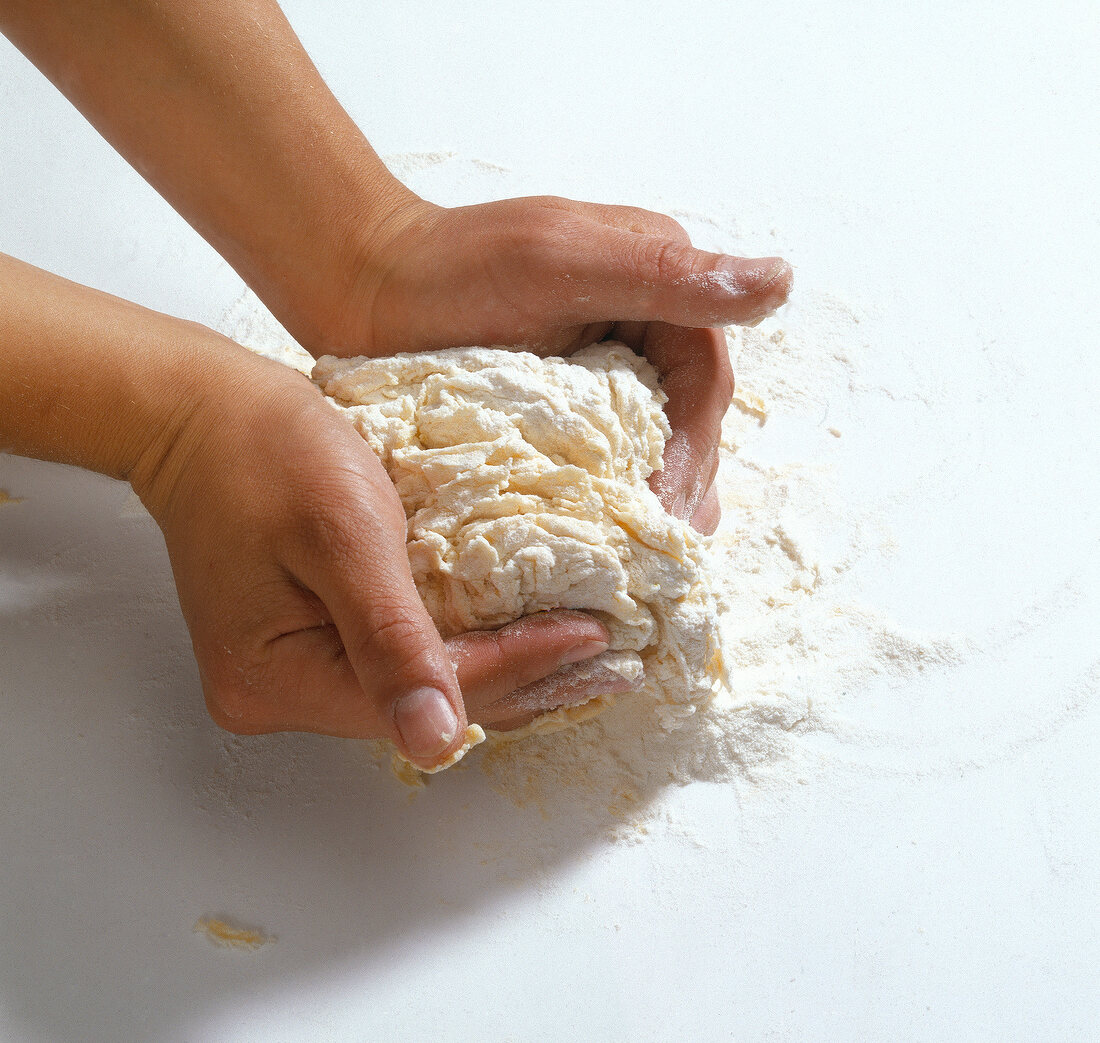 Hand kneading pasta dough on white background
