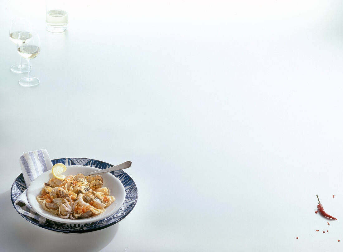 Seafood pasta in bowl with wine glasses on white surface, copy space