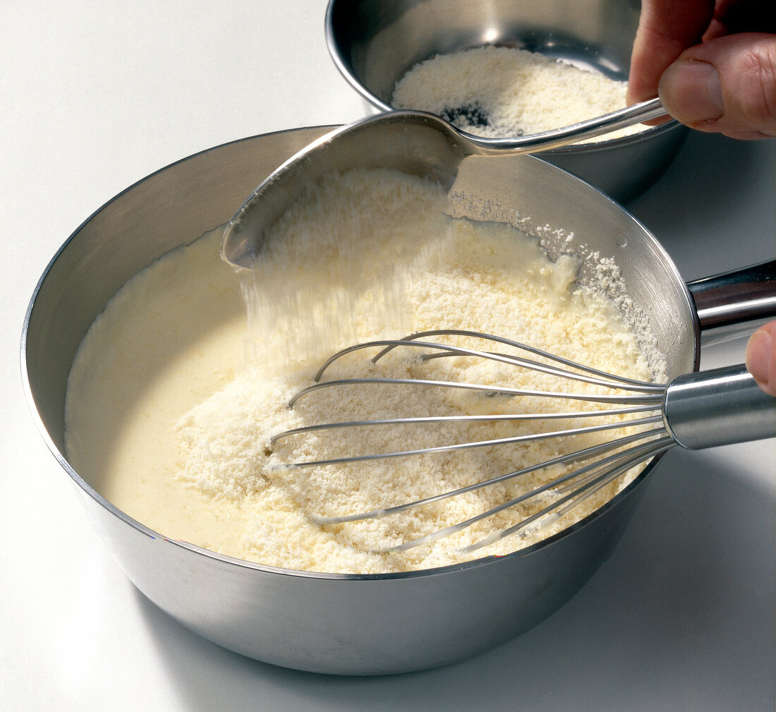 Cheese being added to cream while preparing mornay sauce, step 5