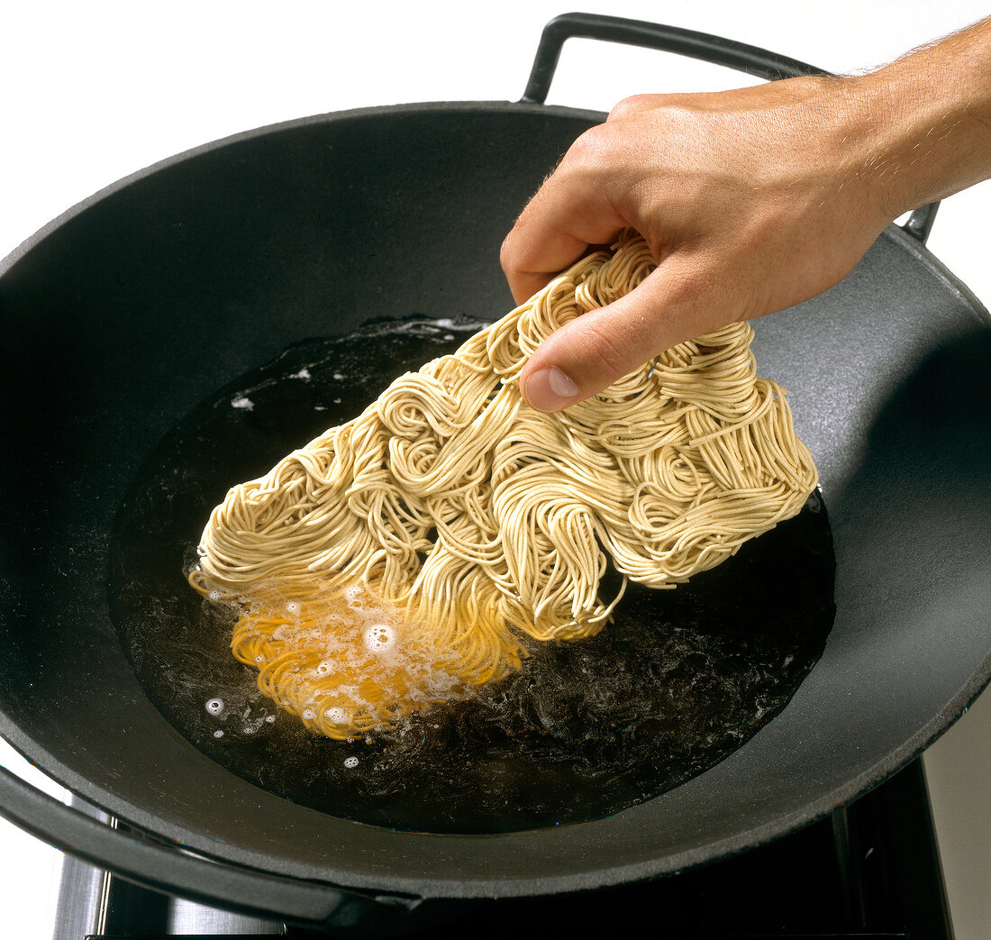 Noodles being added in oil for stir fry in wok, step 1