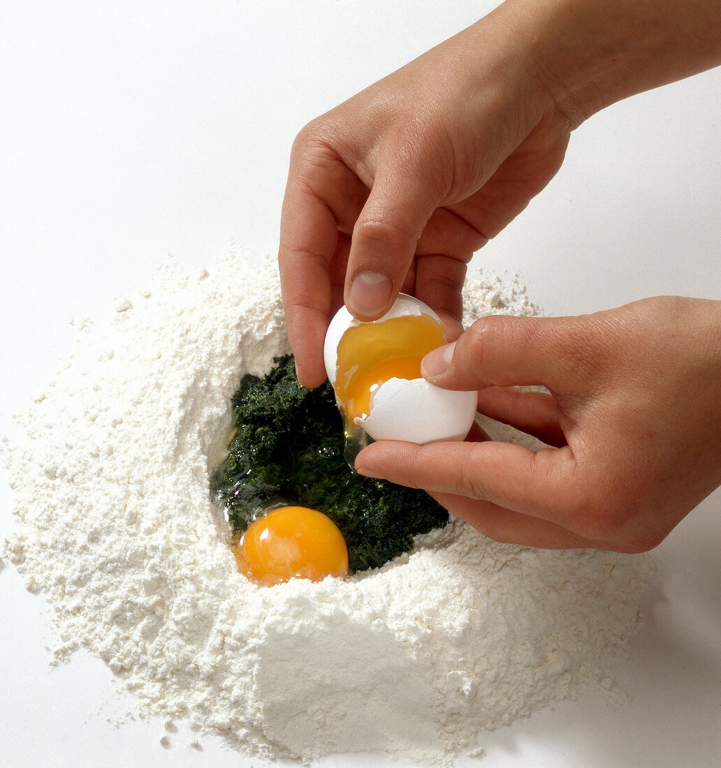 Egg yolks being added to basil paste and flour while preparing herb pasta, step 1