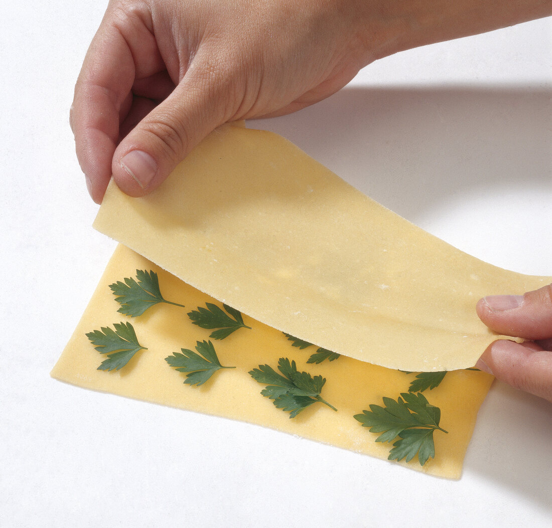 Hand placing pasta layer over another layer with herb, step 2