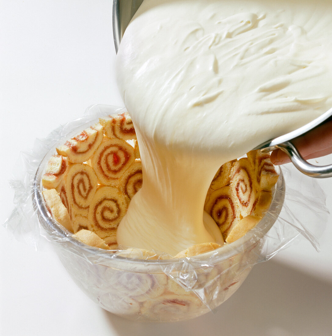 Cream being poured in bowl surrounded with slices of roulade biscuit