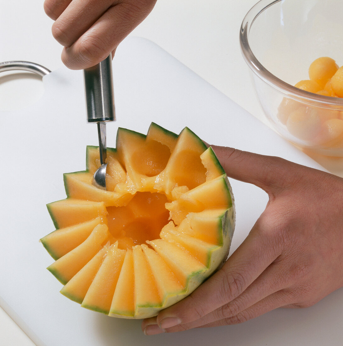 Halved melon being scooped on cutting board