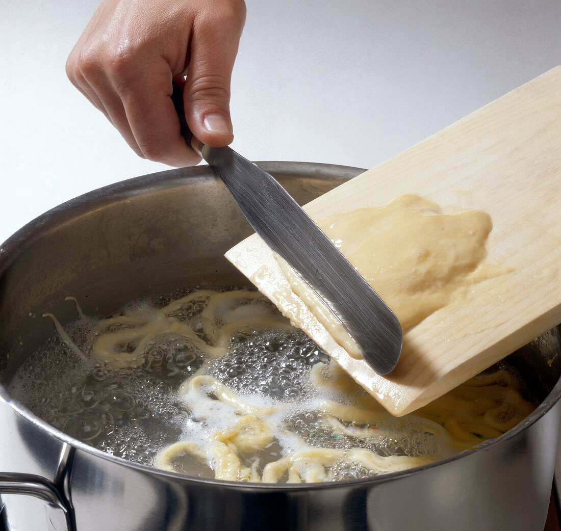 Spatzle being made by adding dough in pot of boiling water