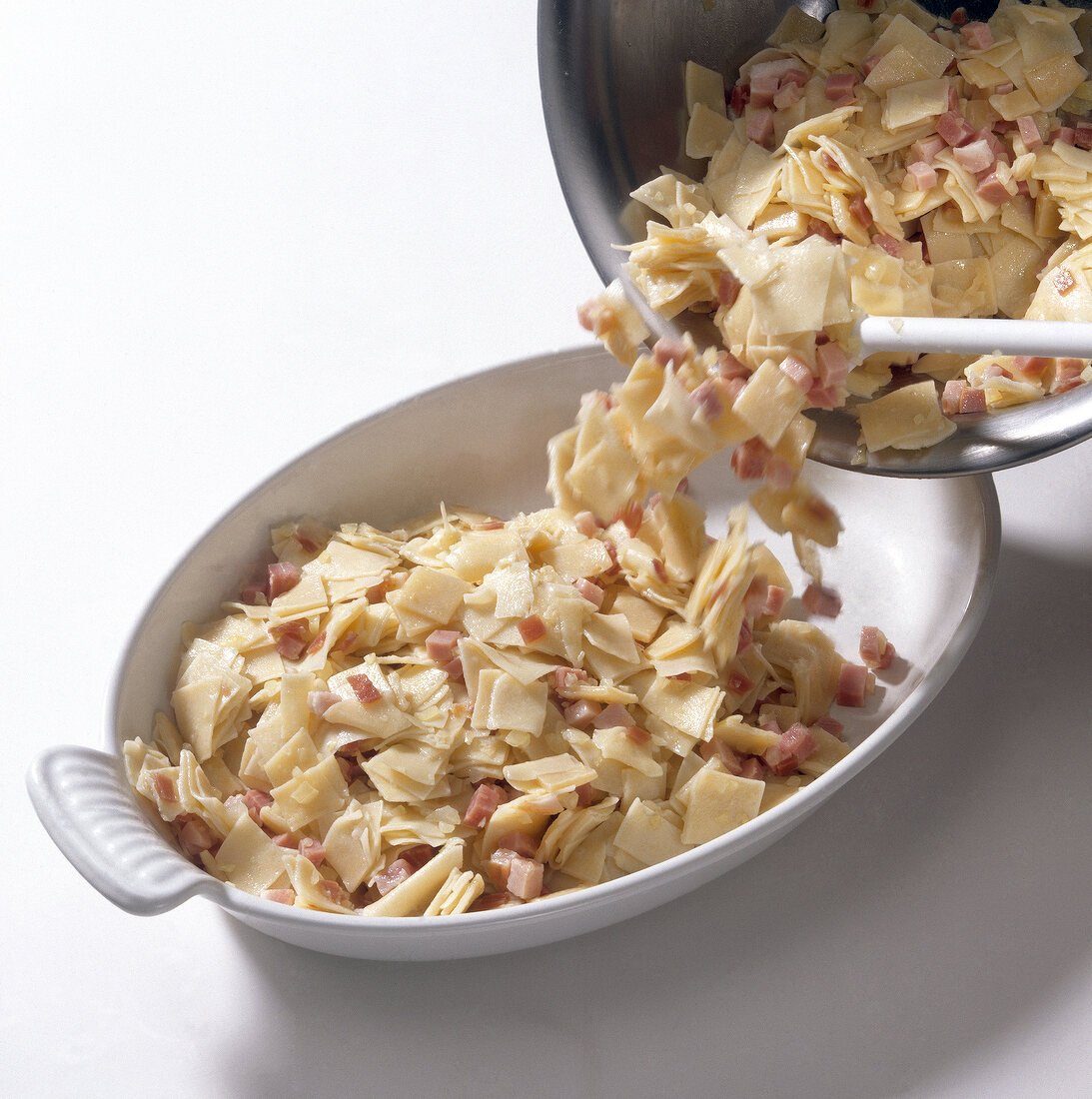 Ham and pasta being put on tray while preparing schinkenfleckerln, step 2