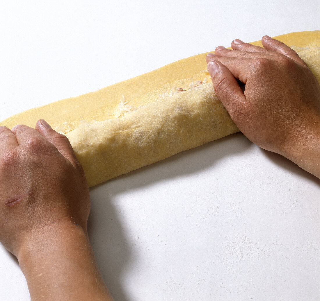 Hands rolling dough with sauerkraut while preparing krautkrapfen, step 4