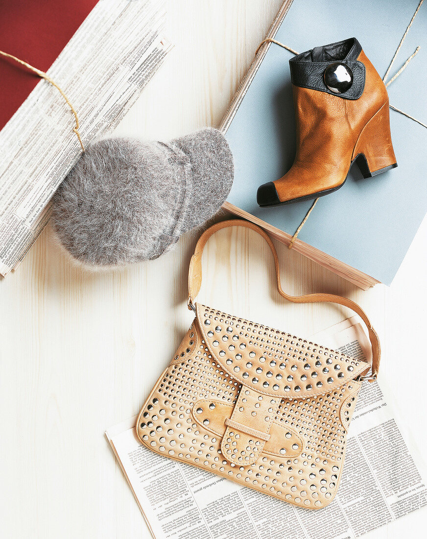 Ankle boots, cap, pile of paper and handbag on wooden flooring