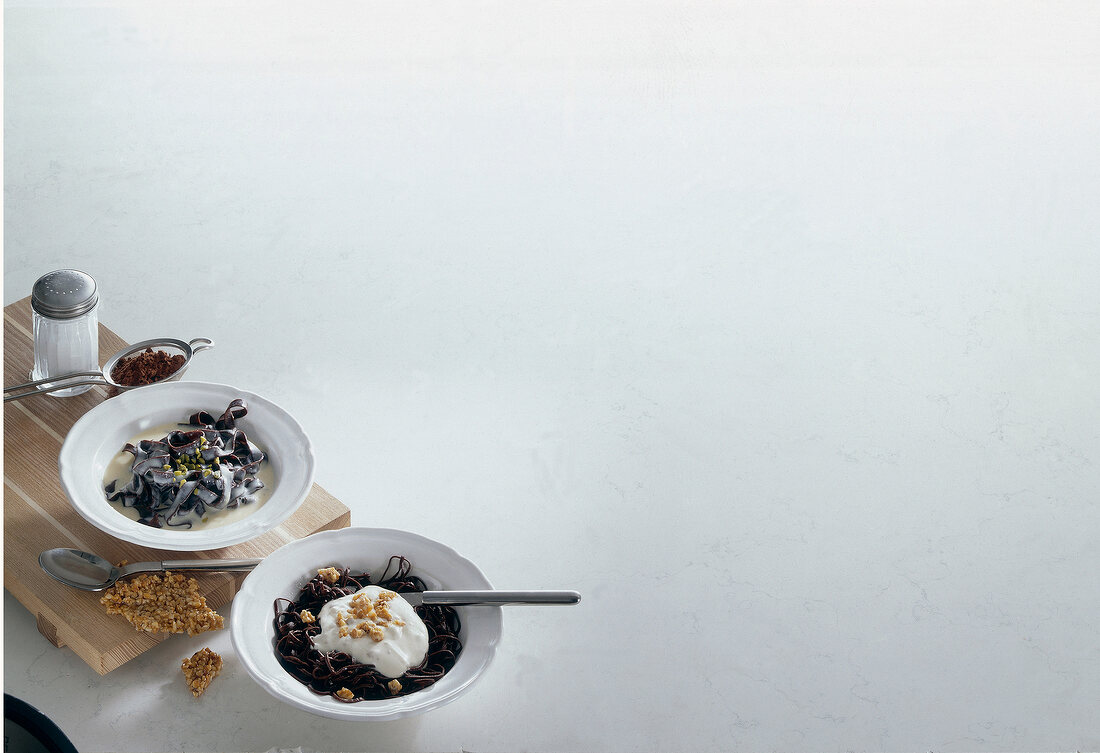 Two bowls of chocolate trenette pasta and trenette pasta with praline cream, copy space