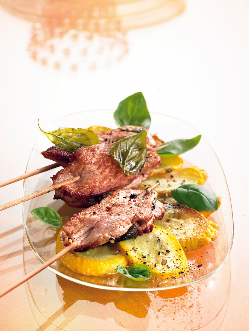 Pork skewer kept on zucchini with basil leaves on glass plate