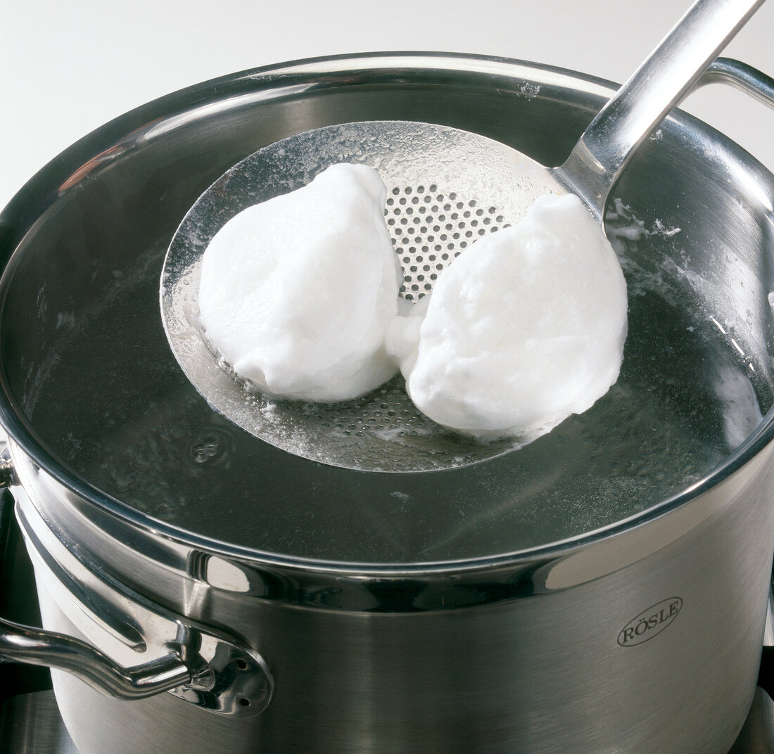 Egg white dumplings being removed from boiling water with trowel