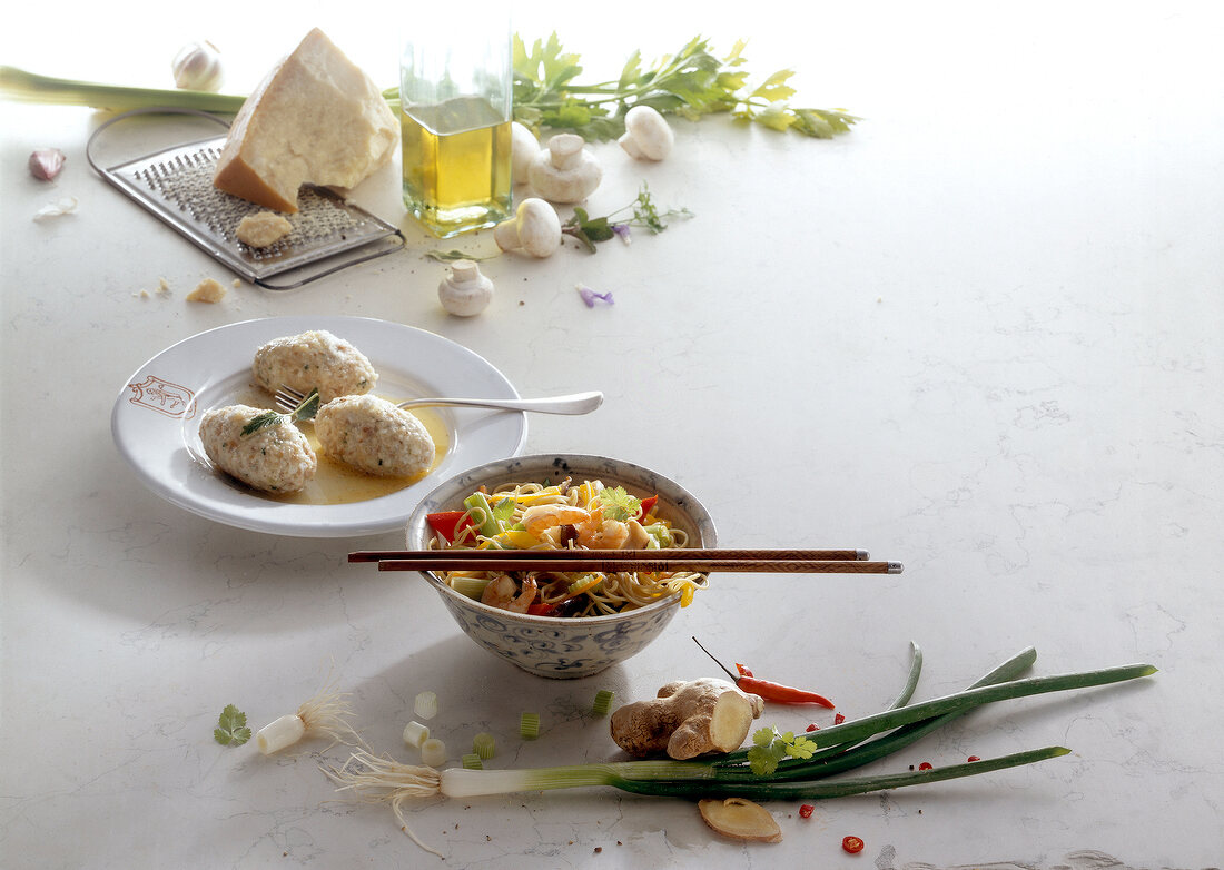 Two types of cooked pasta in bowl with various fresh ingredients on white background