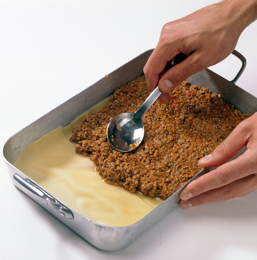 Meat sauce being spread on dough sheet in baking tray