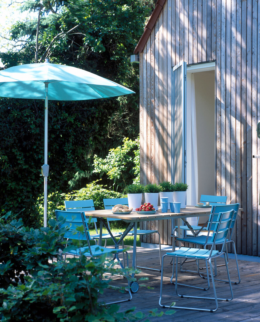 Terrace in front of wooden house with laid table, umbrella and blue chairs