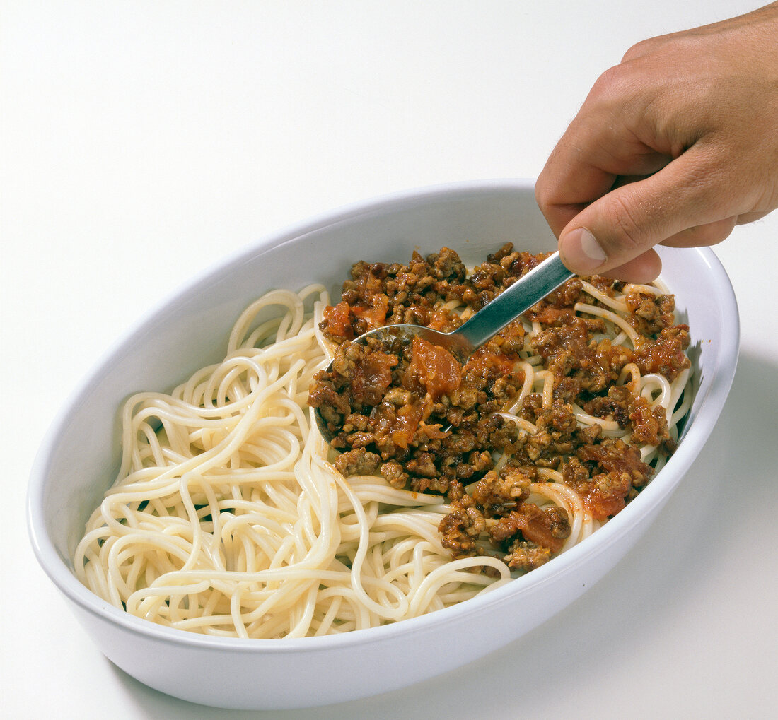 Layer of meat sauce being spread on spaghetti and eggplant slices in baking dish