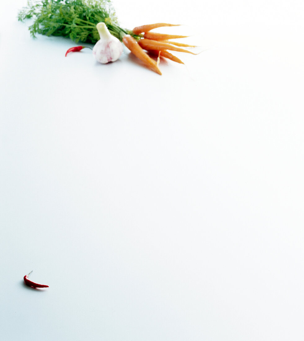 Bunch of carrots and whole clove of garlic with chilli on white background, copy space