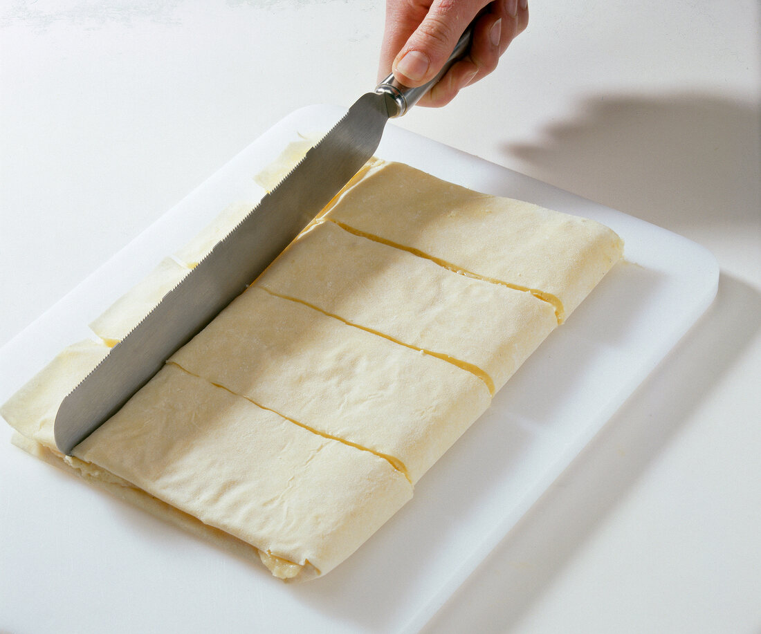Folded dough being cut into rectangles on cutting board