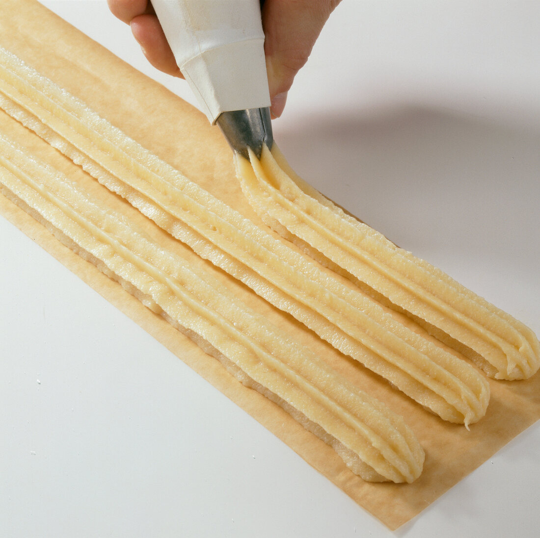 Close-up of strips of dough being made with piping bag on pasta sheet