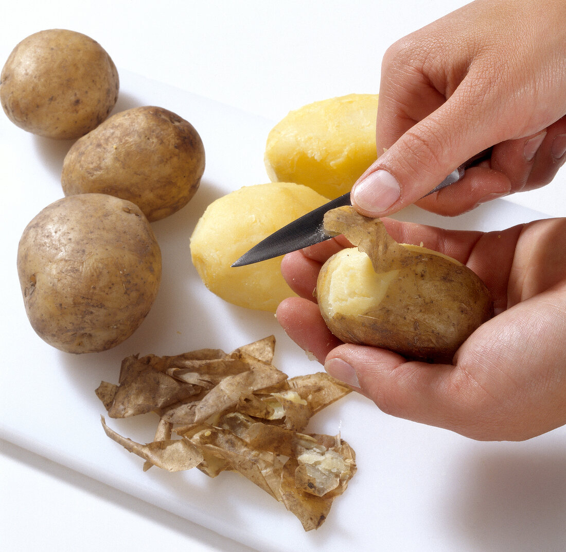 Boiled potatoes being peeled with knife for preparing pasta, step 2