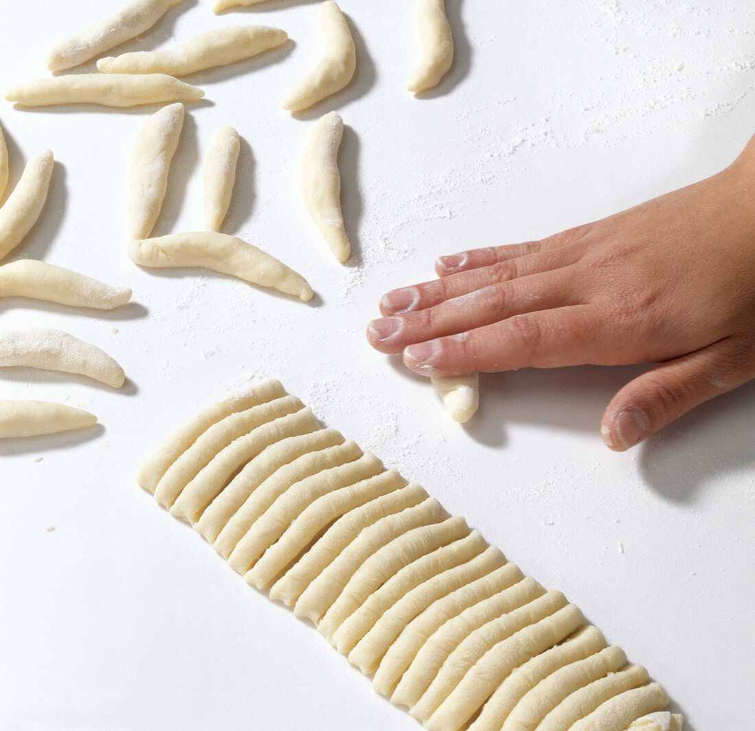 Pieces cut from dough are being rolled with hands while preparing pasta, step 10