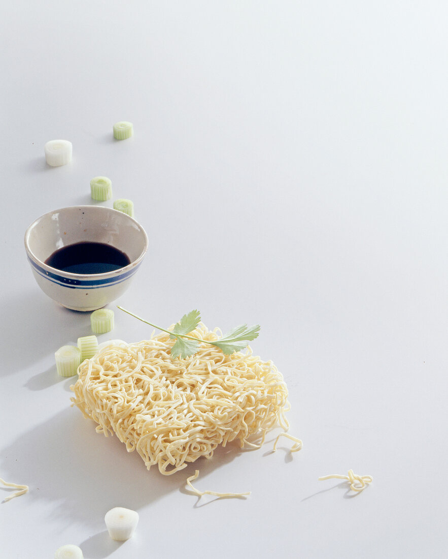 Raw Chinese noodles and sauce in bowl on white background