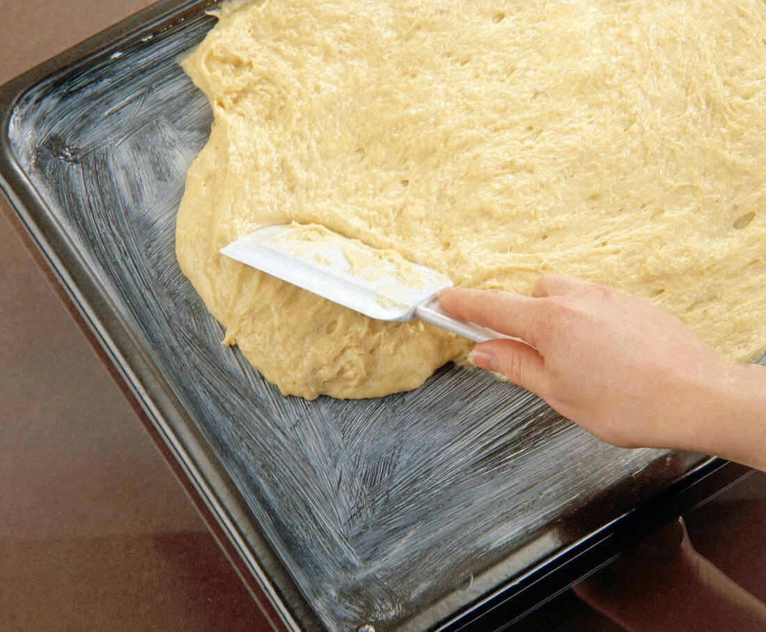 Dough being spread by spatula on butter greased baking tray