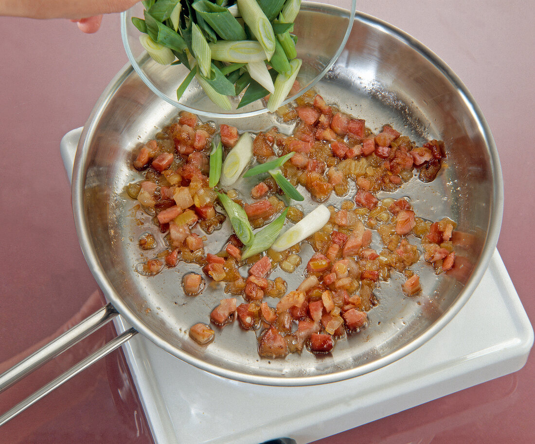 Spring onions with fried bacon in fry pan