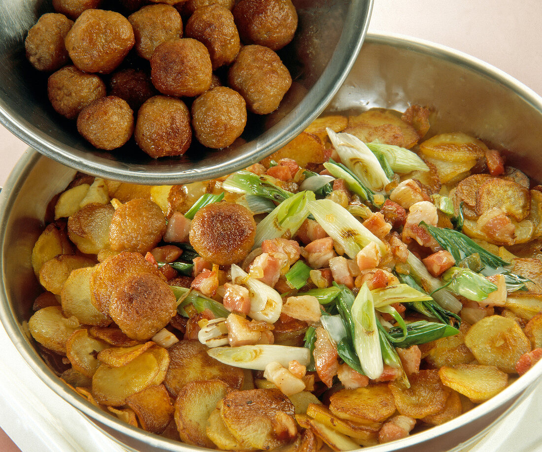 Dumplings with fried potatoes, bacon and green onions in steel pan
