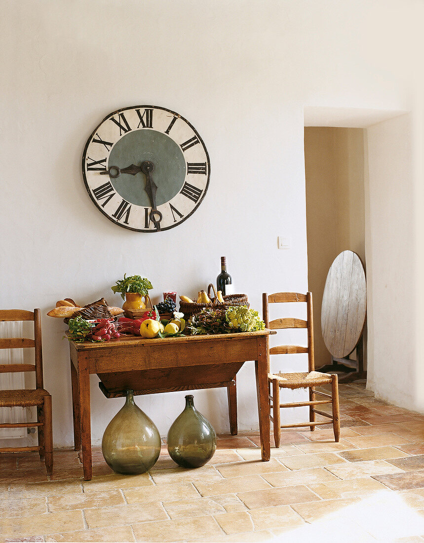 Big clock hanging on wall over table with fruit and vegetables in hallway