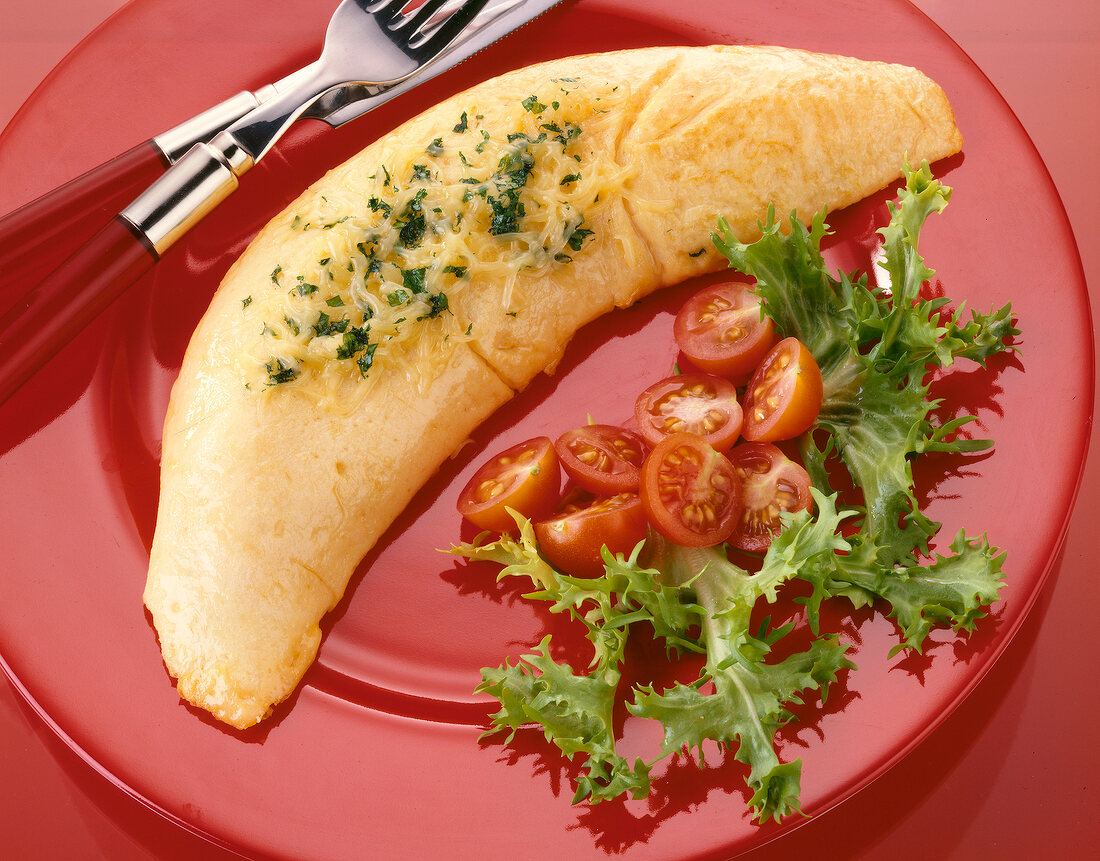 Omelette stuffed with herbs, cheese, tomato and lettuce on red plate