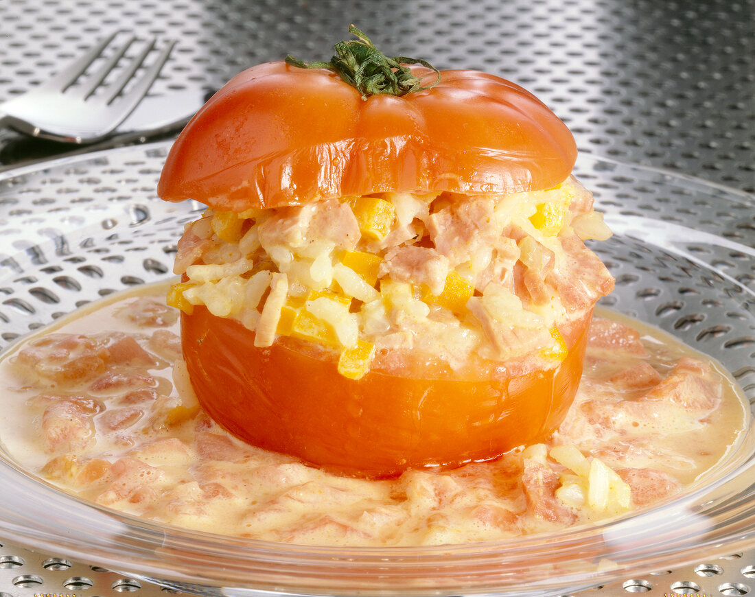 Close-up of stuffed tomato with rice, peppers, ham and egg on glass plate
