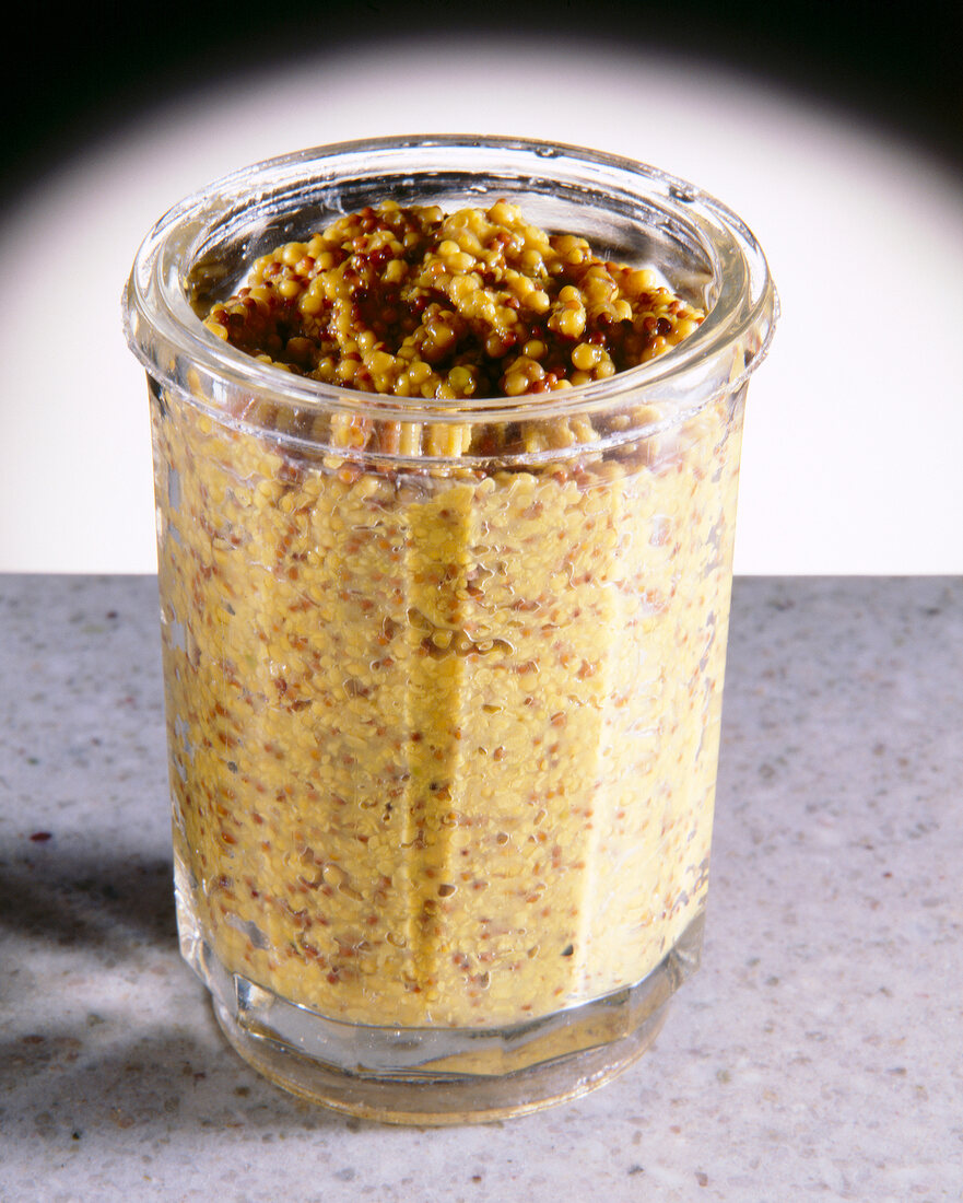 Close-up of yellow brown whole grain mustard in glass jar