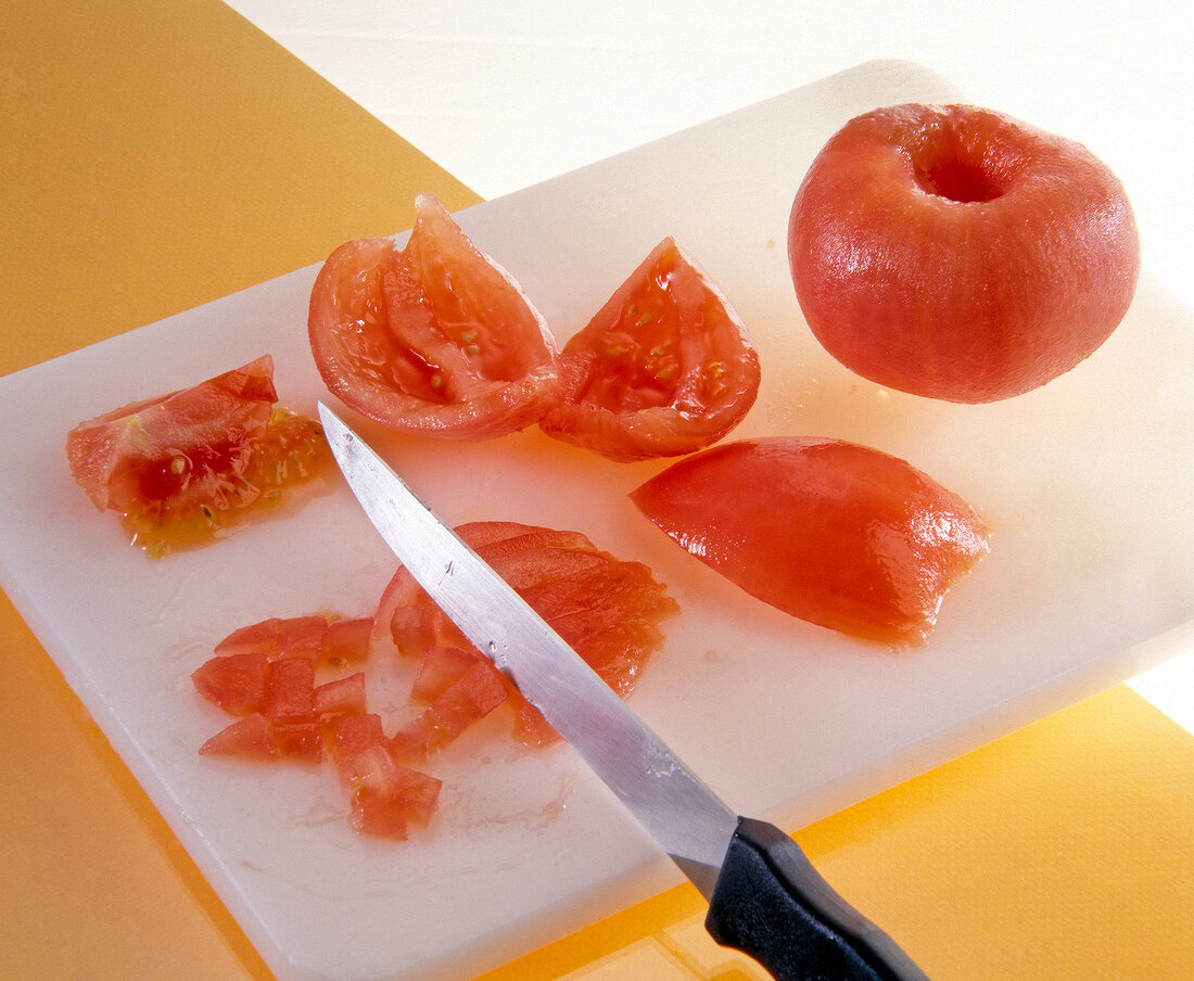 Close-up of tomatoes being cut into cubes on white chopping board
