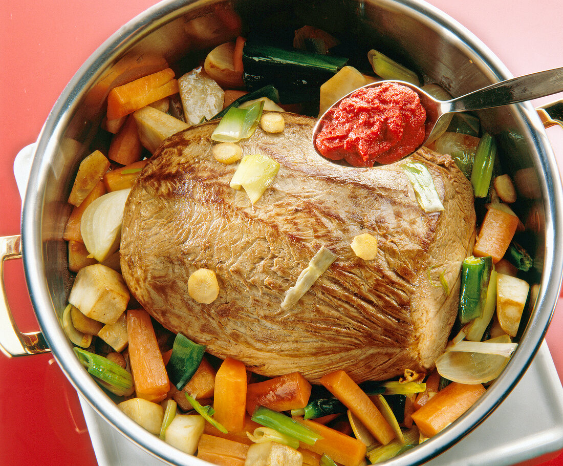 Close-up of tomato paste being added to meat and vegetables in bowl