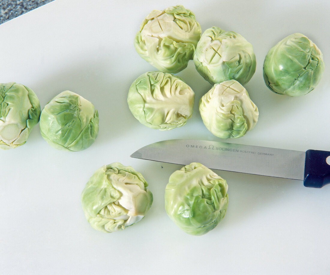 Brussels sprouts with dead leaves cutted on white chopping board with knife
