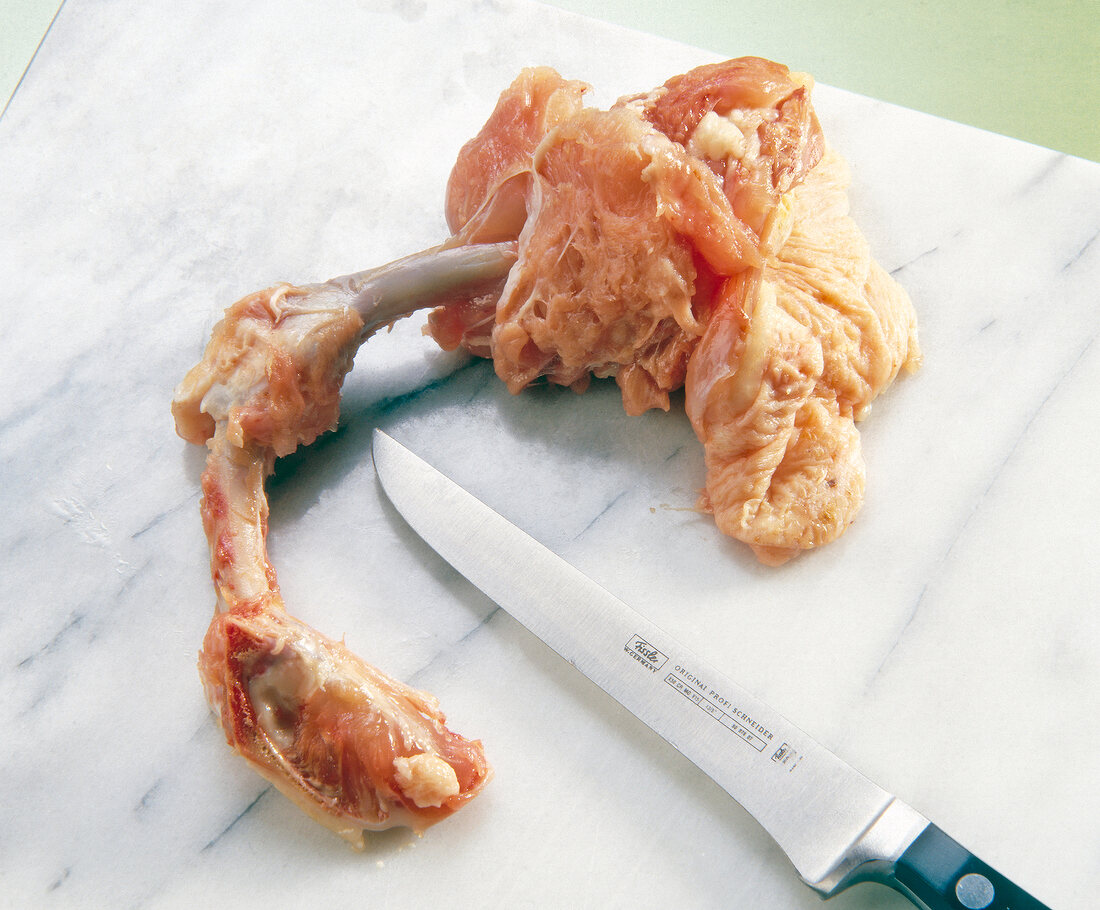 Piece of chicken with knife on chopping board