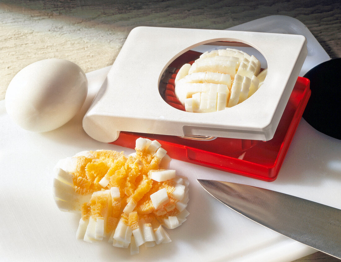 Egg and slices of egg with chopper and knife on white cutting board