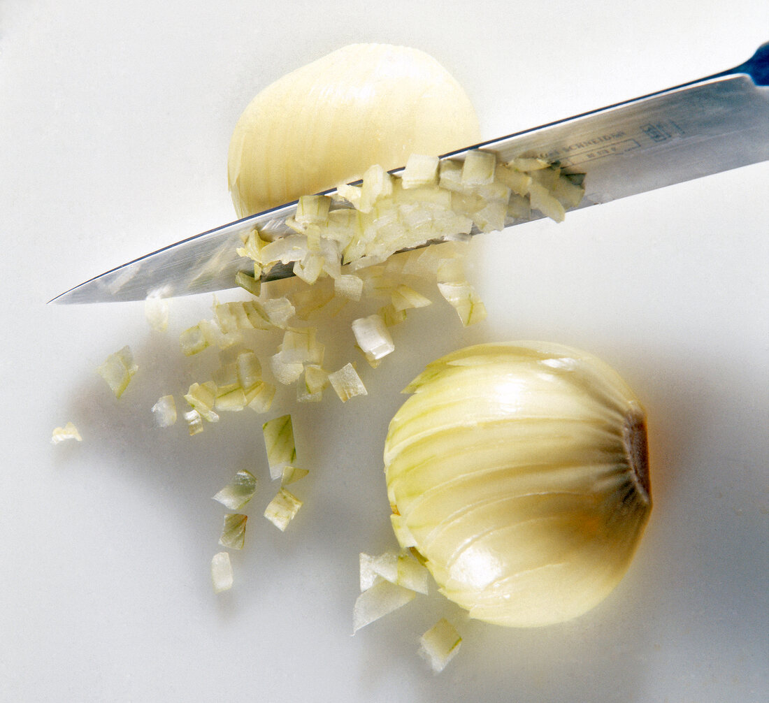 Close-up of onions being chopped with knife into small cubes on white background