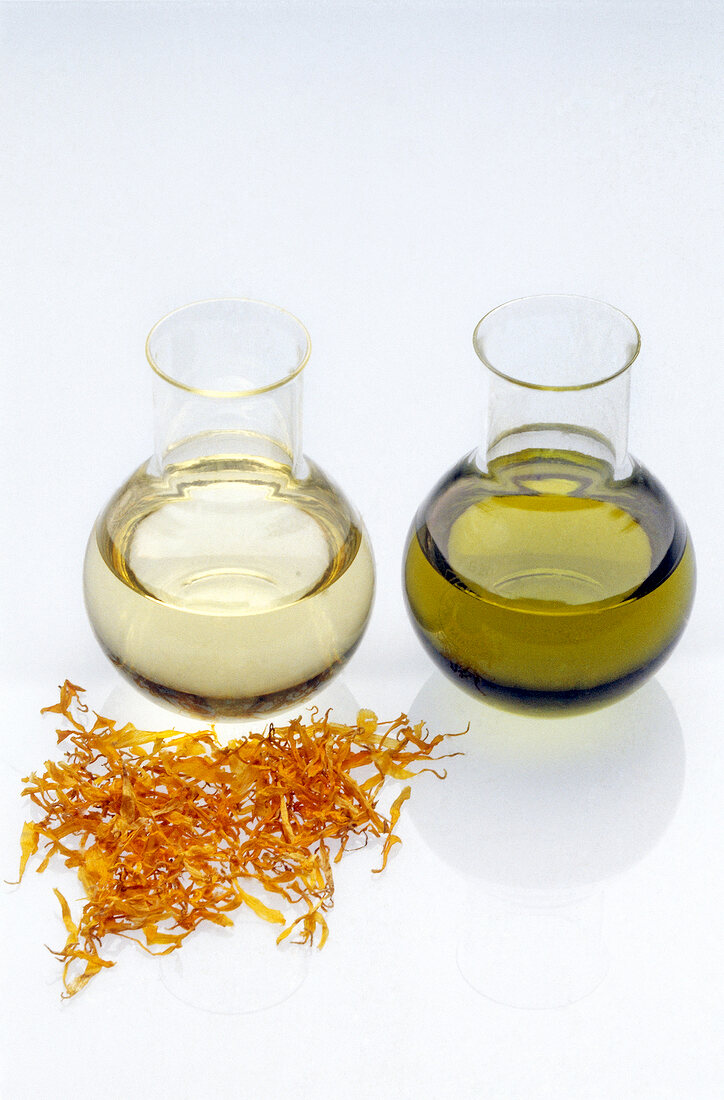 Two flasks containing oil with dried flower petals against white background