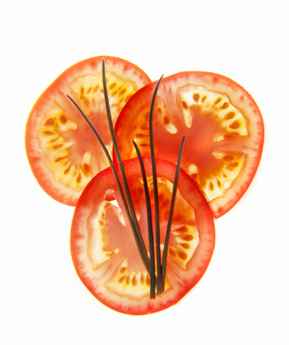 Slices of tomatoes with chives on white background