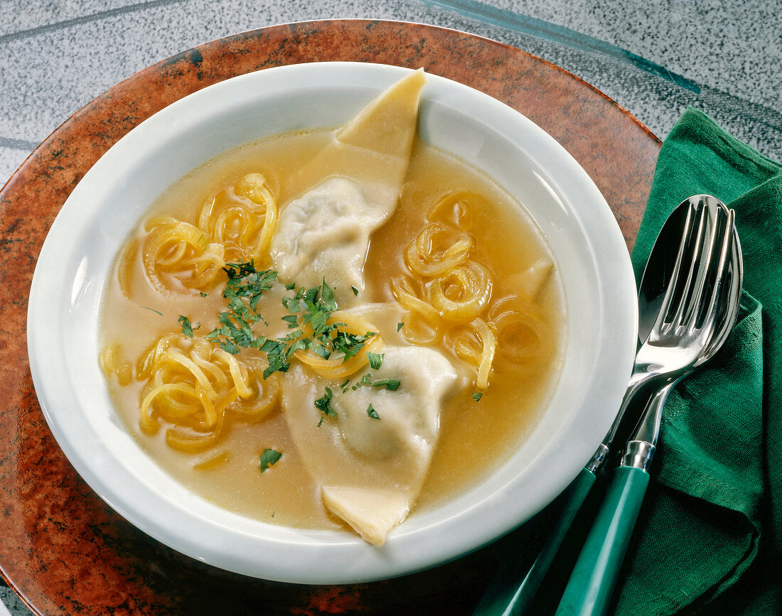 Swabian ravioli with onion broth, spinach and meat filling in bowl