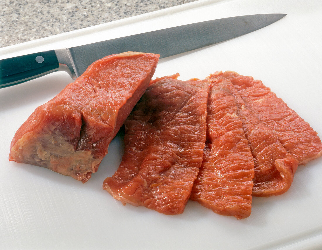 Beef cut in narrow strips with a kitchen knife on a cutting board