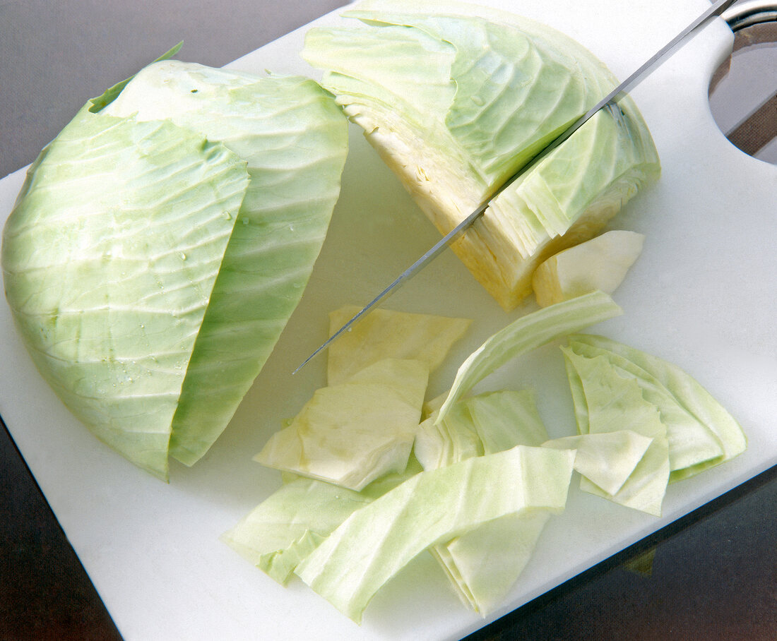 Cabbage cut into slices with knife on cutting board