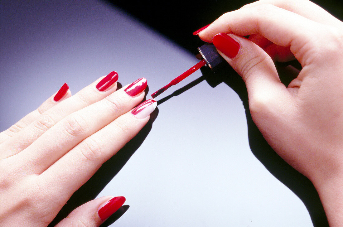 Close-up of woman applying red nail paint on artificial nails, step 3