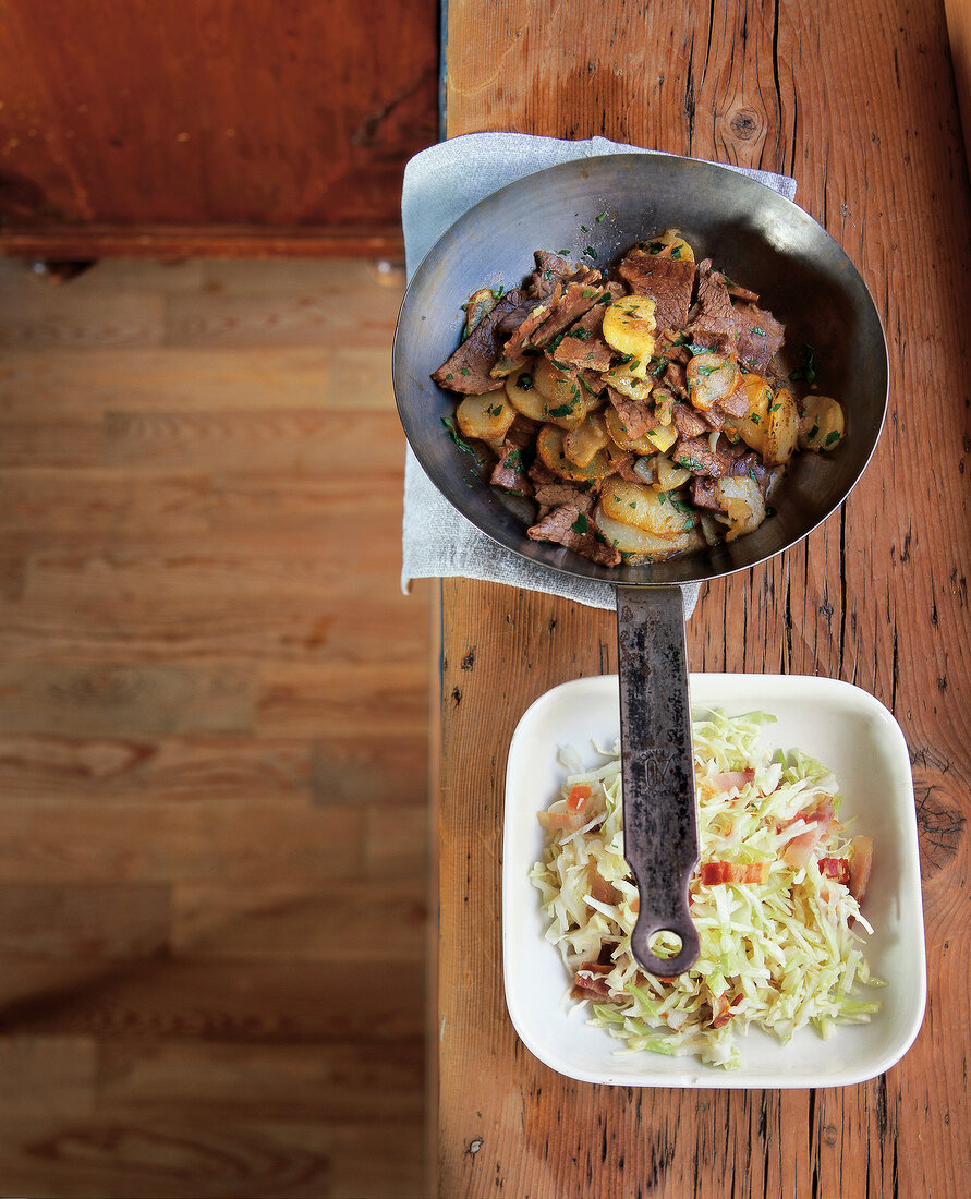 Tyrolean grostl in pan with white cabbage and bacon salad on square plate