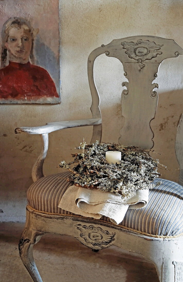Adventskranz mit einer weißen Kerze auf einem alten Stuhl