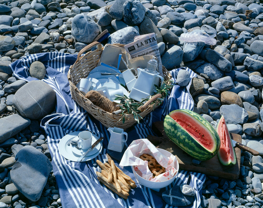 Blanket with picnic basket and food on stone beach