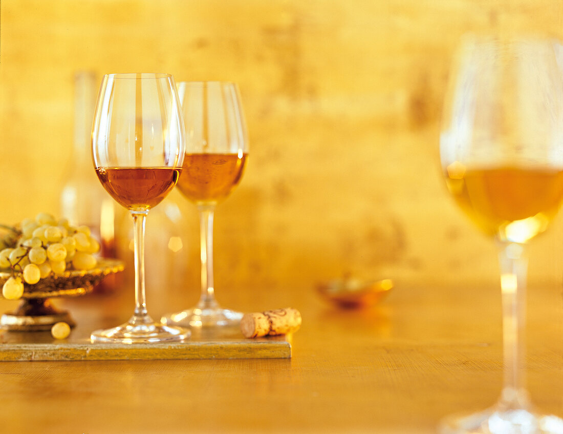 Three glasses of wine besides grapes on orange background