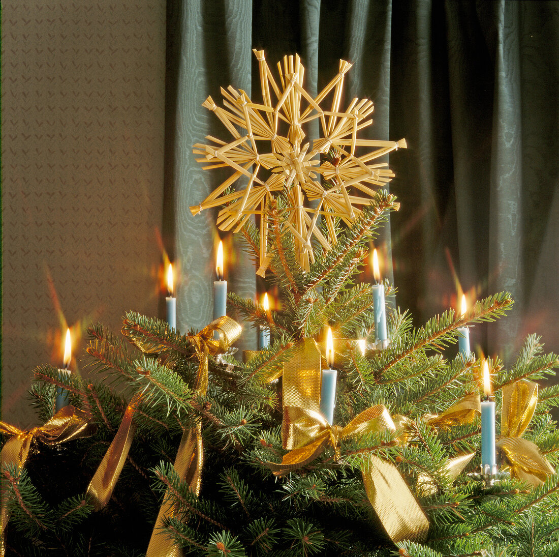 Strohstern als Christbaumspitze am Tannenbaum mit brennenden Kerzen
